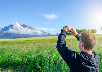 Male tourist photographs a mountain landscape on a smartphone.