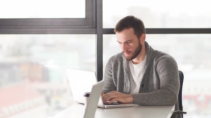 Concentrated european young clerk in spectacles looking at the laptop.