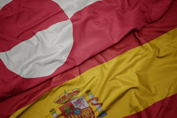 waving colorful flag of spain and national flag of greenland.