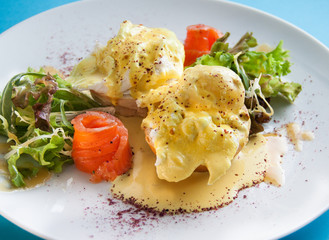 Egg benedict with smoked salmon, lettuce salad mix and hollandaise sauce on bread. On plate