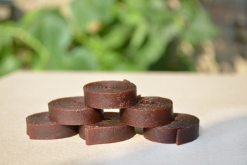 Pieces of round pastille rolled up in pyramid shape on brown cardboard paper with shadows from sun on green background
