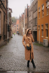 Stylish woman in brown coat standing on the bridge in Bealgium, Brugge. Female put on a hood