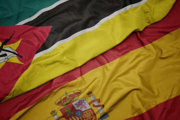 waving colorful flag of spain and national flag of mozambique.
