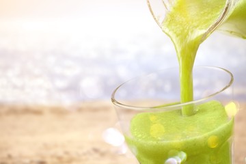 Green smoothie in a clear glass beaker on the beach background