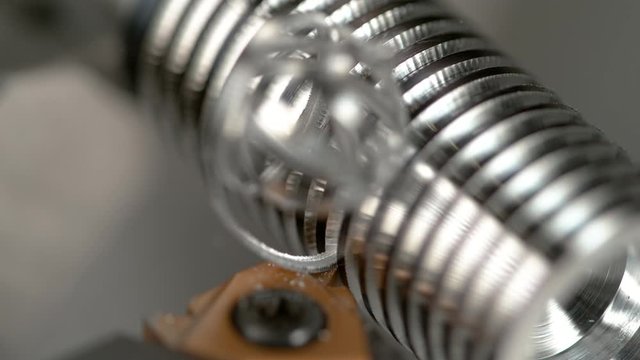 SLOW MOTION, MACRO, DOF: Curly shavings break off a small metal rod being processed by CNC equipment into a screw. Sharp cutter carving deep grooves into a silver workpiece during threading process.