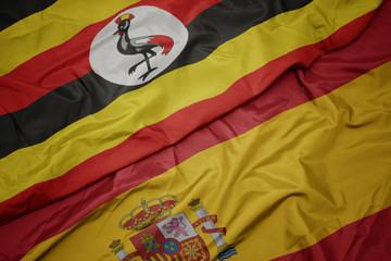 waving colorful flag of spain and national flag of uganda.