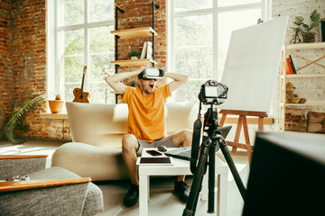 Full of emotions. Caucasian male blogger with professional camera recording video review of VR glasses at home. Blogging, videoblog, vlogging. Man using virtual reality headset while streaming live.