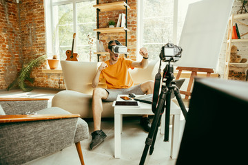 Full of emotions. Caucasian male blogger with professional camera recording video review of VR glasses at home. Blogging, videoblog, vlogging. Man using virtual reality headset while streaming live.