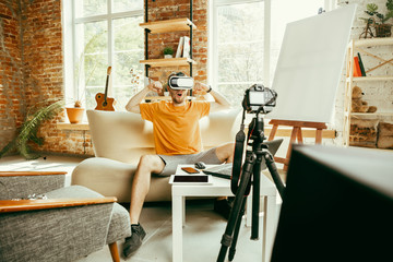 Full of emotions. Caucasian male blogger with professional camera recording video review of VR glasses at home. Blogging, videoblog, vlogging. Man using virtual reality headset while streaming live.