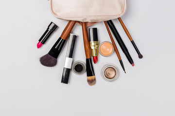 A pink makeup bag with cosmetic beauty products spilling out on to a light  background, with empty space at side