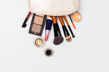 A pink makeup bag with cosmetic beauty products spilling out on to a light  background, with empty space at side