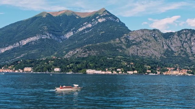 Scenic shot of a boat floating on Como lake near the coastline and mountains in Lombardy, Italy