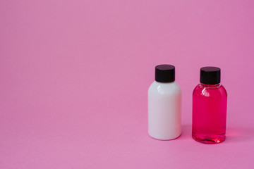 front view of small white and pink bottles on a pink background. Cosmetics on the road for skin care or hair. Copy location