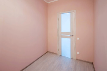 Empty small room with whitewashed floating laminate flooring and newly painted pink wall in background