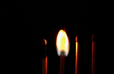 Four wooden matches on a black background. Two unlit, one burning, one burning.