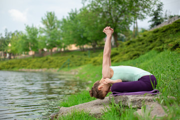 Slim brunette girl doing yoga in the summer on a green lawn by the lake