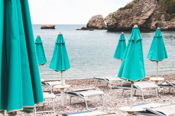 Turquoise umbrellas, white sunbeds, beach, sea.The end of the summer season. Closed turquoise umbrellas and white sunbeds on the beach.