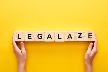 cropped view of woman holding wooden blocks with legalize lettering on yellow background