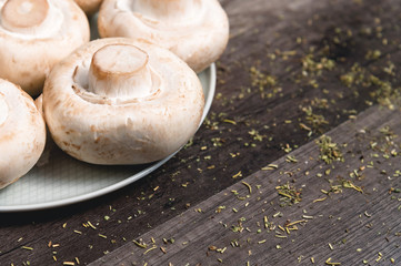 Close-up of white mushrooms on a white plate on a dark wooden table. Vegetarian healthy food