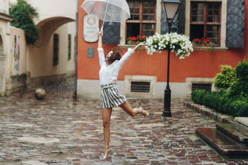 Woman tourist walks around the city, playing with her umbrella. It's summer rain.