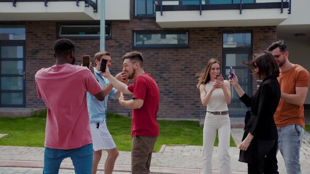 Modern generation. Group of best friends hanging out together taking pictures and videos on smartphones to have fun while walking in the street. Fun and entertainment.