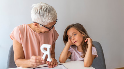 Little girl with teacher on private lesson. A child with development problems with a professional speech therapist during a meeting. Tutor holding a letter 'R'.