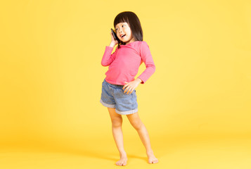 Fototapeta na wymiar Portrait of a cute Asian little girl, talking on the phone, isolated on yellow background