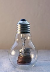 Pile of metal coins in a glass light bulb. Concept of saving electricity and associated finance.