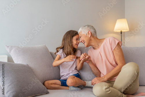 Happy middle-aged mature grandma and little preschool granddaughter touching noses laughing together, smiling loving old grandmother granny and cute carefree grandkid girl having fun playing at home