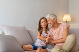 Granddaughter kissing grandmother on cheek in living room. Grandmother's give the best hugs. Little cute girl and her grandmother are spending time together at home.
