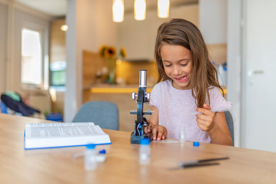 Little girl concentrates while using microscope. Studying chemistry. Confident little girl uses microscope at home. Schoolgirl using microscope.