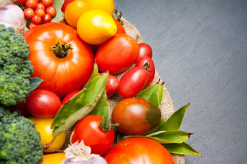 Tomatoes, broccoli, garlic on a black background with burlap with place for text