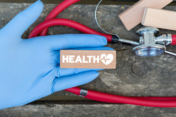 Health word with heart rate icon on wood block in doctor's hand and stethoscope. Healthcare concept.