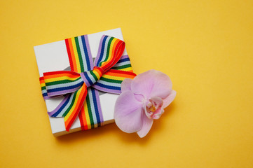 white gift box with rainbow ribbon and Orchid flower on yellow background copy space the concept of pride