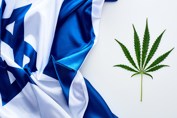 top view of green cannabis leaf near flag of Israel on white background
