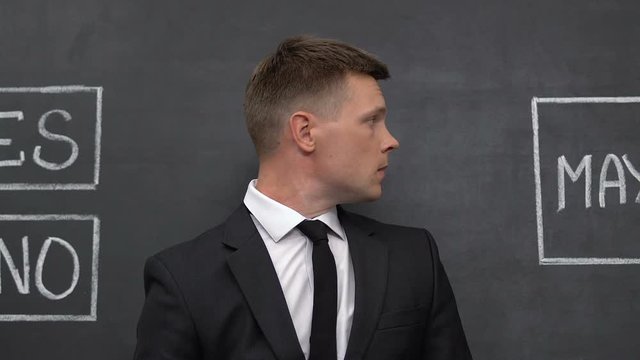 Businessman feeling puzzled, looking on yes, no and maybe words written, choice
