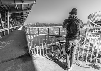 man with the bicycle and backpack on the bridge in winter (black and white)
