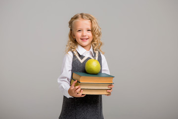 little blonde girl in school uniform with Apple and books on light background,first-grader smiling on a white background