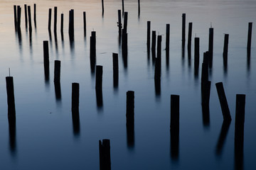long exposure of wood pilings in blue ocean water at dusk