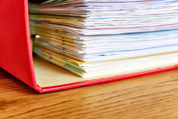 Red ordner with papers. Stack of business papers, bills or documents in ordner document binder closeup on wooden desk. Debt free life, business office stress workload or paperless office concept. 