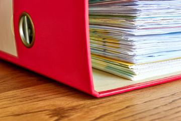 Red ordner with papers. Stack of business papers, bills or documents in ordner document binder closeup on wooden desk. Debt free life, business office stress workload or paperless office concept. 