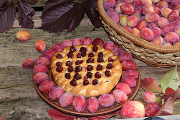 Plum and cherry tart, plum basket and fallen autumn leaves, top view, flat lay, selective focus. Plum pie on an old wooden background in the garden background,