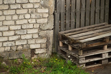 old pallets under a fence near a brick wall