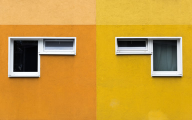 Fototapeta na wymiar A pair of two windows on a yellow and orange facade