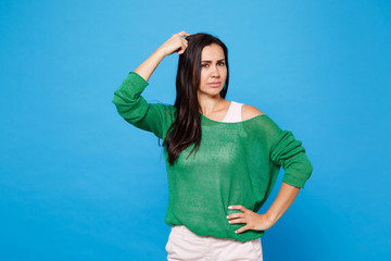 Portrait of preoccupied puzzled young woman in green casual clothes looking aside, putting hand on head isolated on bright blue wall background in studio. People lifestyle concept. Mock up copy space.