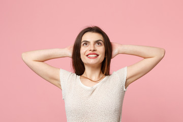 Pensive young woman in casual light clothes posing isolated on pink background, studio portrait. People sincere emotions lifestyle concept. Mock up copy space. Looking up with hands behind her head.