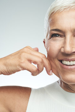 Gorgeous smiling Caucasian senior woman with short gray hair pinching her cheek. Beauty photography.