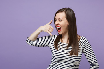 Cheerful young woman girl in casual striped clothes posing isolated on violet purple background. People lifestyle concept. Mock up copy space. Looking aside doing phone gesture like says call me back.