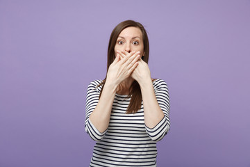 Shocked young brunette woman girl in casual striped clothes posing isolated on violet purple wall background studio portrait. People lifestyle concept. Mock up copy space. Covering mouth with hands.