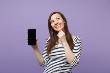 Young brunette woman in casual striped clothes posing isolated on violet purple background studio portrait. People lifestyle concept. Mock up copy space. Hold in hand cellphone with blank empty screen